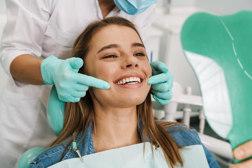 a young woman sits smiling in a dental chair after discovering what are the benefits of a smile makeover