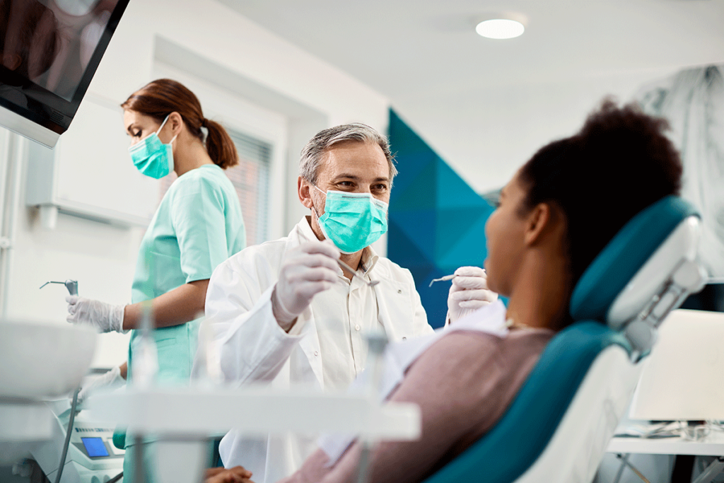 young woman reclined in dental chair surrounding by dental professionals explaining why oral cancer screening is important.