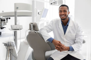 smiling male dental professional seated next to dental chair explaining what does a dentist specialized in restoration do?